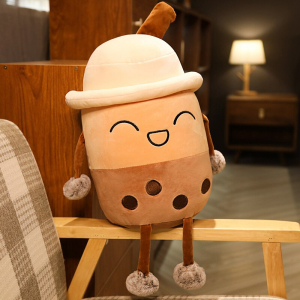 Bubble tea plysch skrattar med en hatt, hon är beige och brun och sitter på träarmstödet i en beige, vit och brun rutig fåtölj i en lägenhet med en lampa tänd i bakgrunden