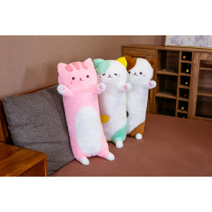 På en grå soffa i ett litet vardagsrum med brunt golv, 3 plyschkuddar med en stor katt som står på soffan, en är rosa, den andra är grön och den tredje är brun
